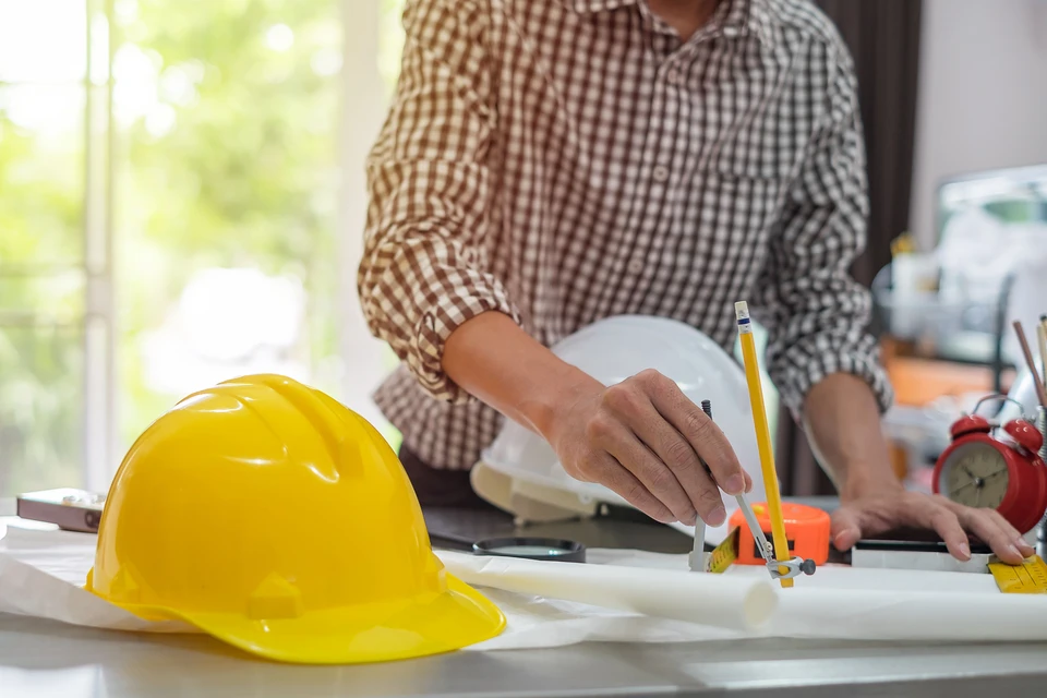 Photographie d'un chantier de construction de bâtiment de santé en cours de finition, montrant une équipe de construction composée de plusieurs professionnels (architecte, maître d'œuvre, ouvriers spécialisés) discutant devant les plans du projet. L'image doit montrer la collaboration et l'expertise collective, avec en arrière-plan une structure architecturale moderne et professionnelle en phase de finition intérieure. L'atmosphère doit transmettre la coordination technique, la maîtrise professionnelle et l'accompagnement personnalisé d'un projet de construction spécialisé.